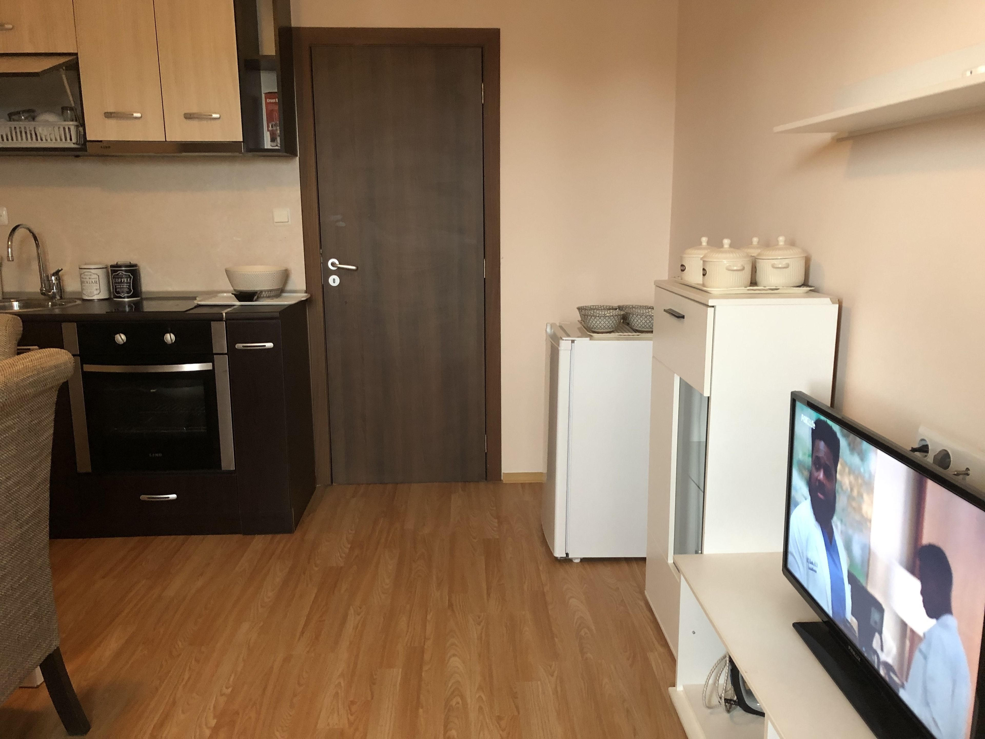 A compact kitchen with a refrigerator, oven, and a TV displaying a scene.