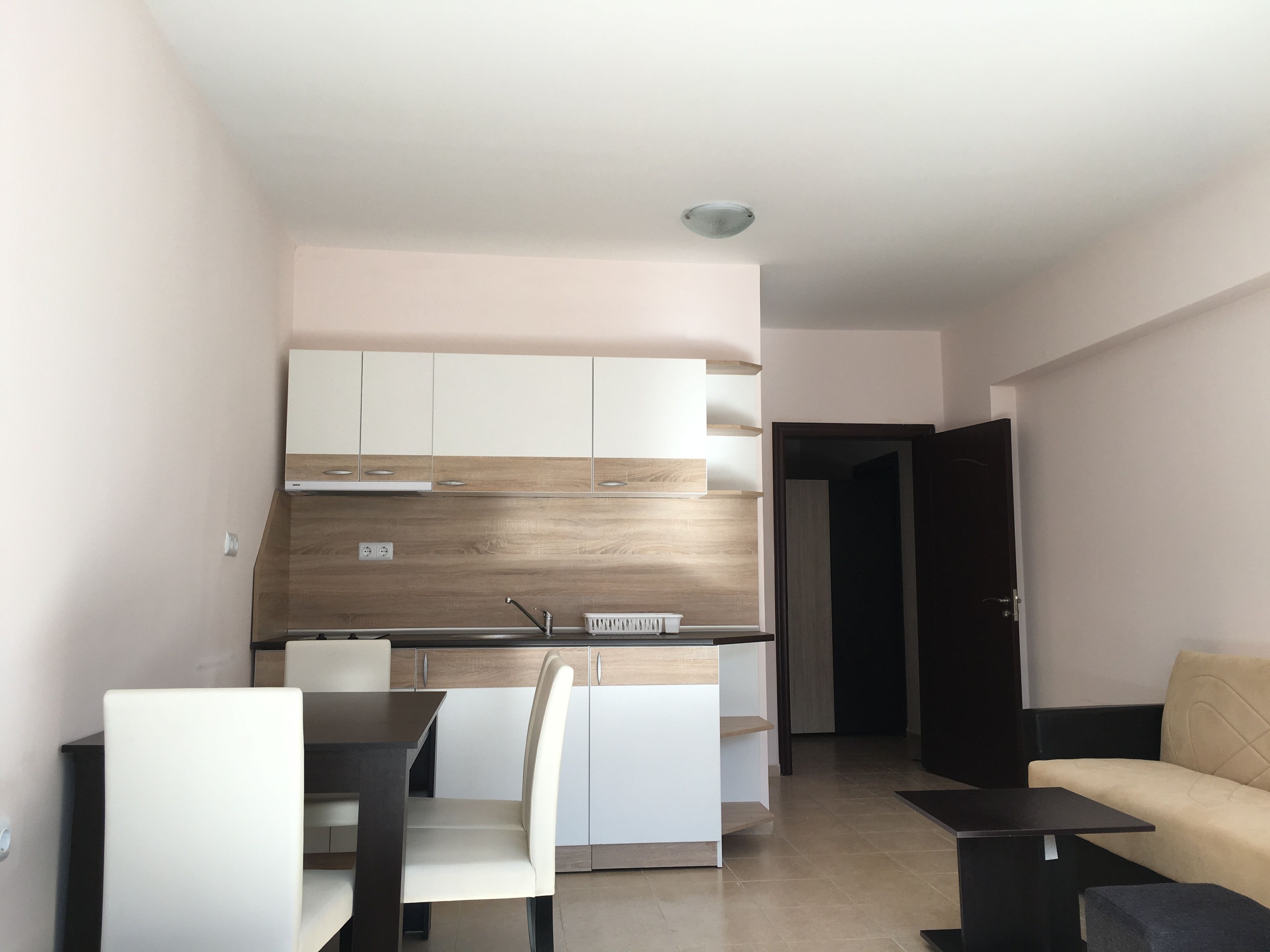 Una cocina moderna con armarios blancos, encimera de madera y horno empotrado. Hay un comedor con mesa y sillas, y un sofá en la sala de estar.