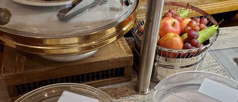 A buffet area with a cake, fruit, and two bowls of cream.