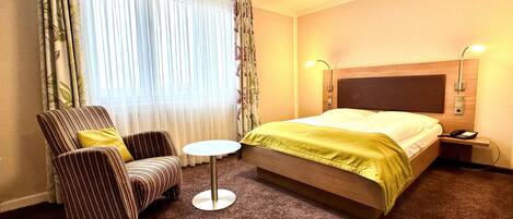 A hotel room with a bed, a chair, a small table, and curtains.