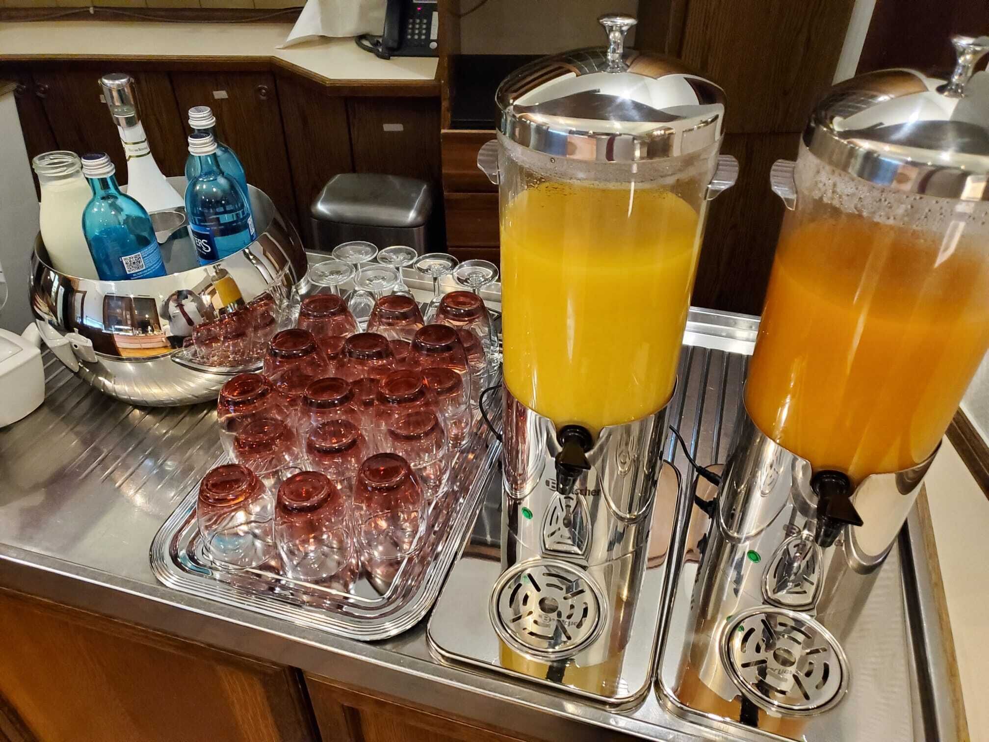 Una estación de bebidas con varios dispensadores y una bandeja de vasos.