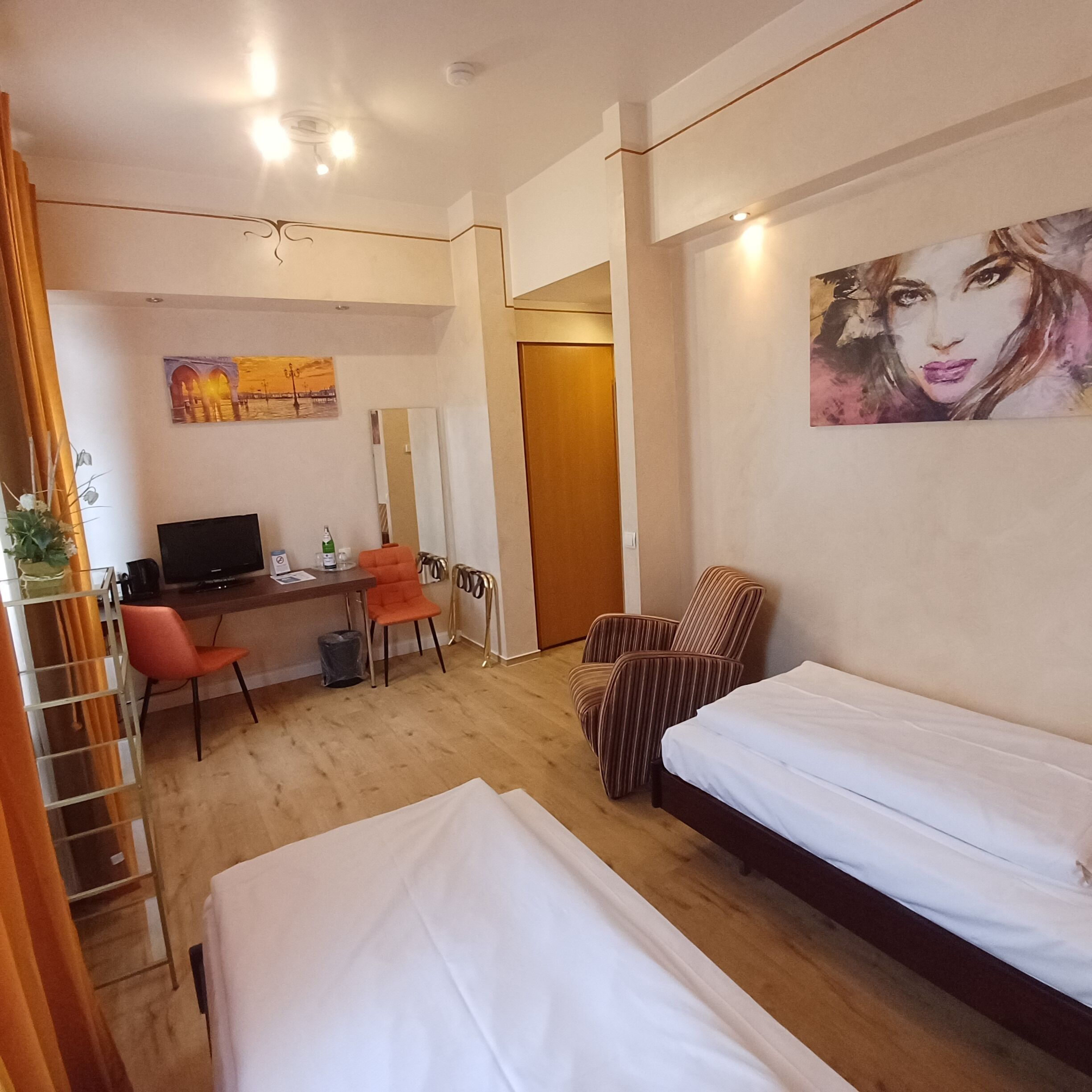Ein Hotelzimmer mit einem Bett, einem Schreibtisch mit Computer, einem Stuhl und einem Bild an der Wand.