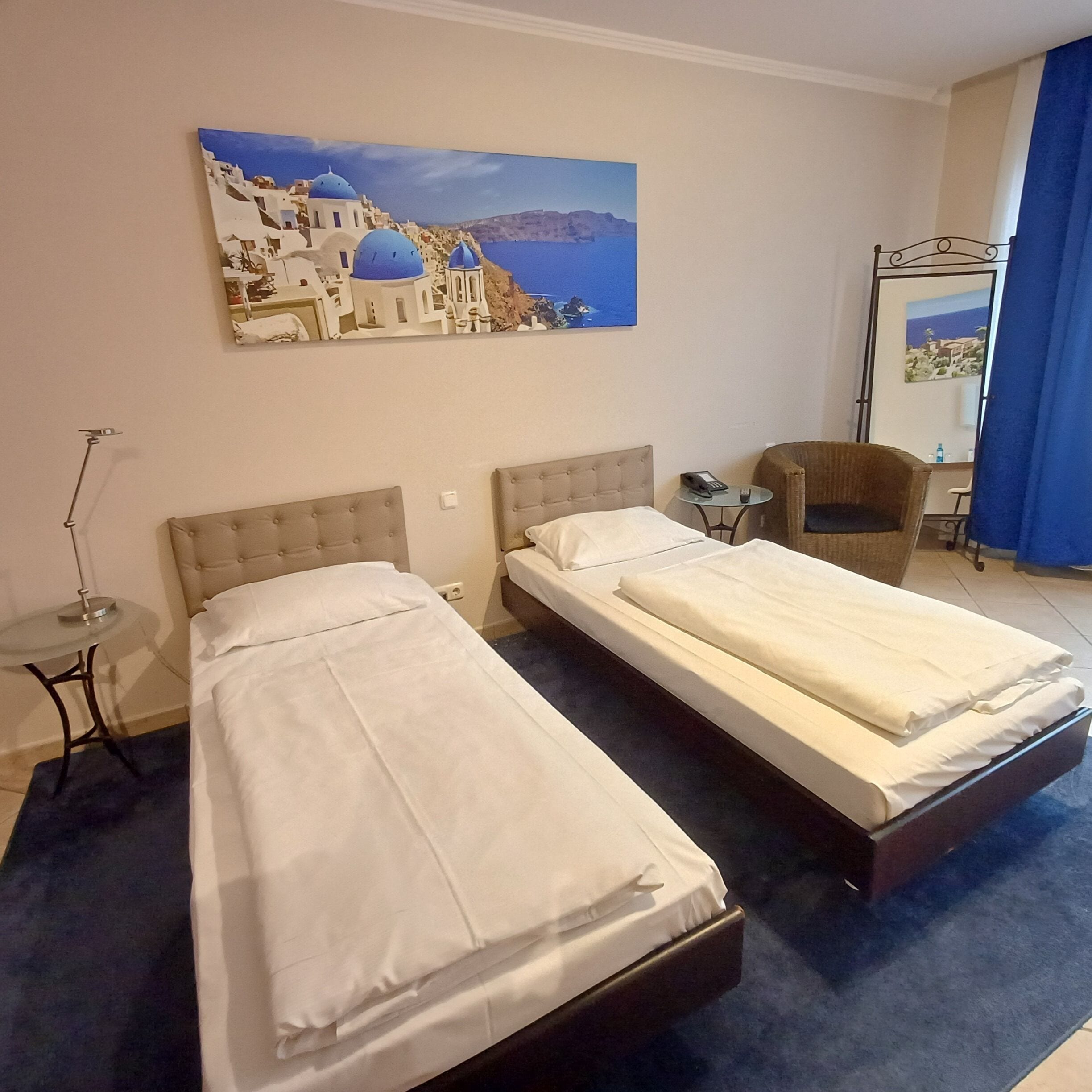 Camera d'albergo con due letti, un tavolino, una sedia e un quadro raffigurante una costa.