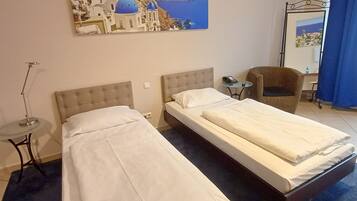Camera d'albergo con due letti, un tavolino, una sedia e un quadro raffigurante una costa.