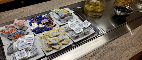 Uma mesa de buffet com diversos alimentos, incluindo queijo, iogurte e picles.