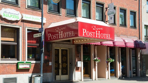 Un hôtel avec un auvent rouge et une enseigne sur laquelle on peut lire « PostHotel ».