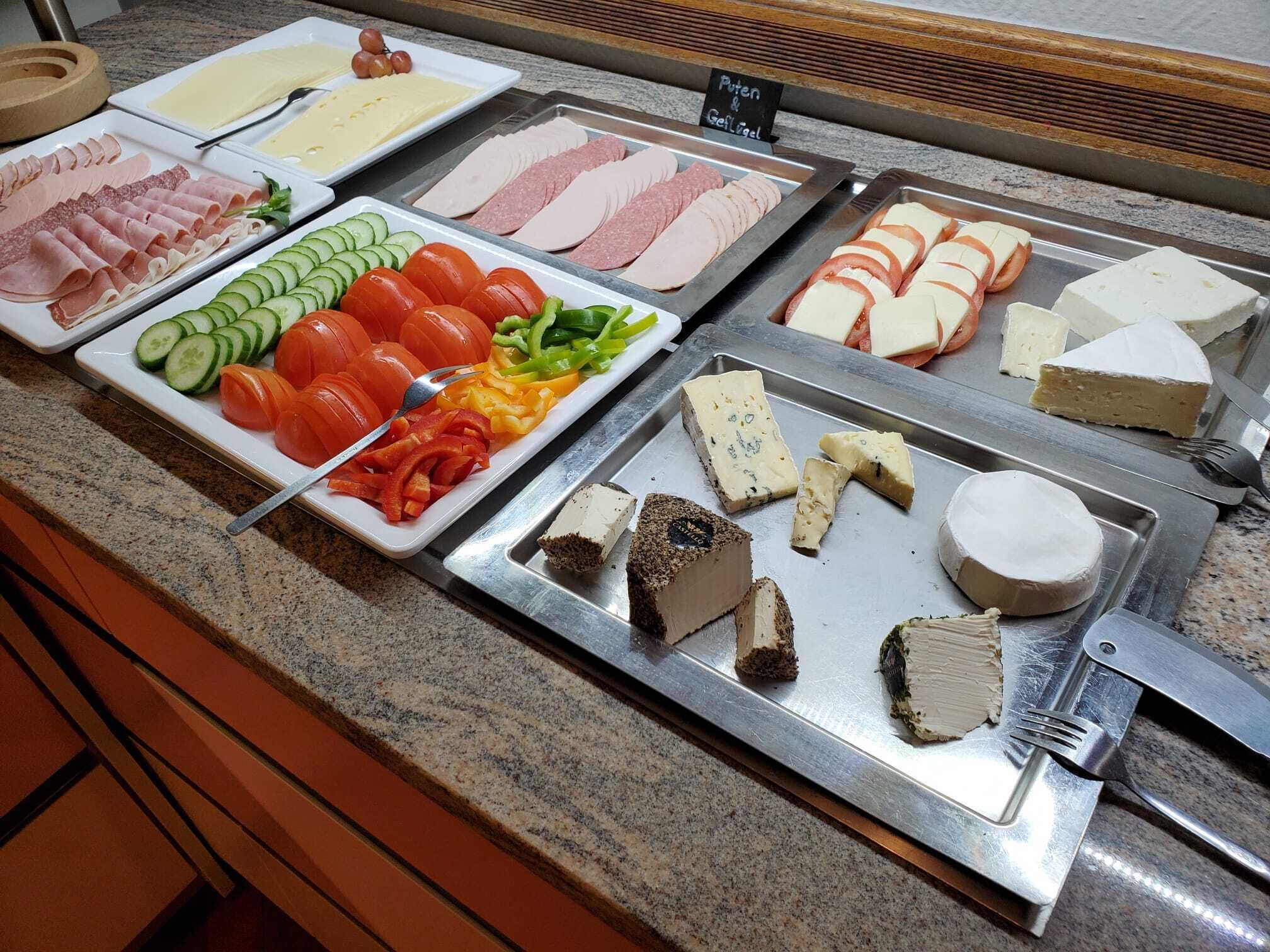 Un bufé con diversas opciones de comida, incluyendo carnes, quesos y vegetales.