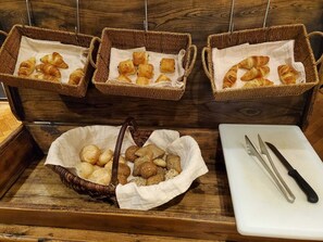 Tres cestas de mimbre con pasteles y una cesta de palitos de pan sobre una encimera de madera.