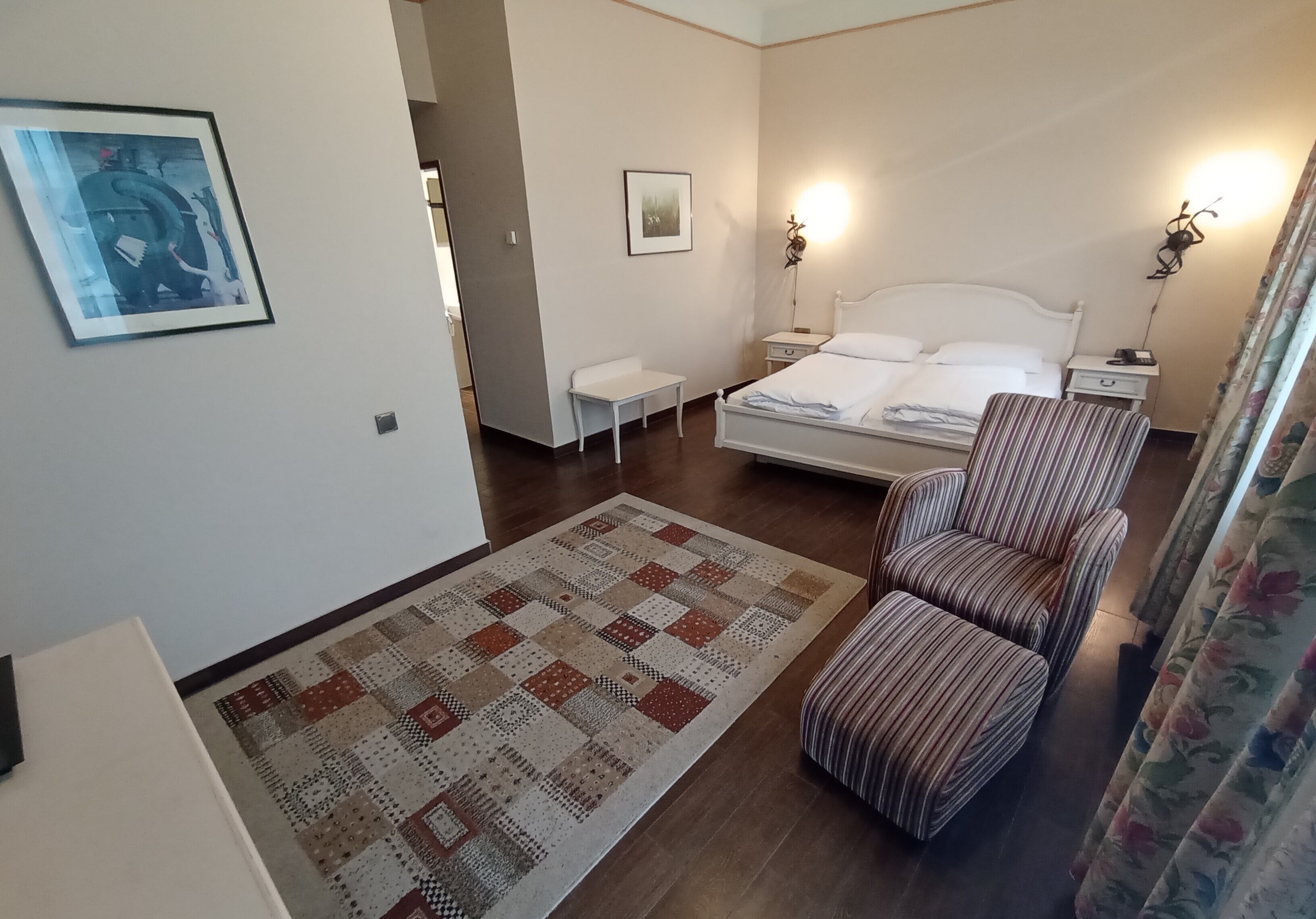 A bedroom with a bed, a bedside table, a chair, a rug, and two wall-mounted lamps.