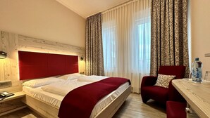 Une chambre d’hôtel avec un lit en bois, une tête de lit rouge, un bureau avec une chaise et une bouteille d’eau sur la table de chevet.