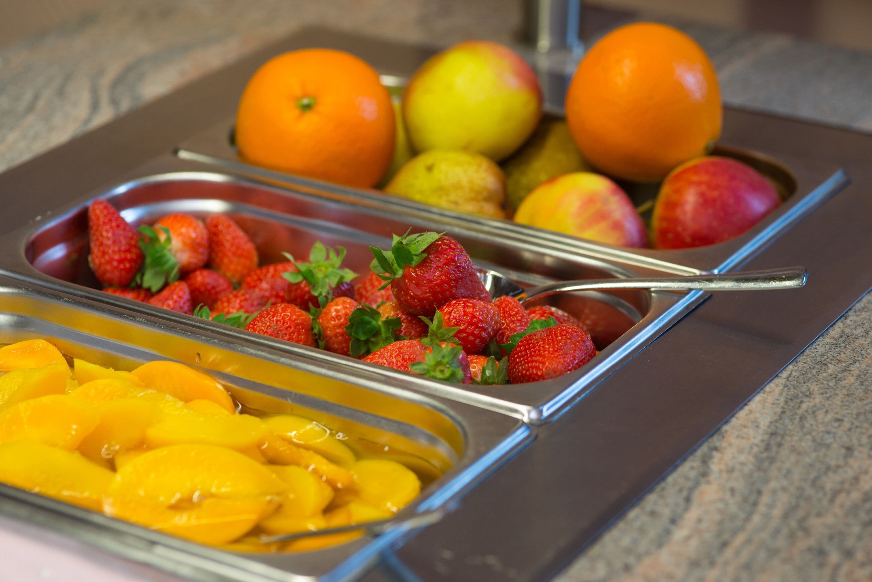 A buffet with various fruits including strawberries, peaches, oranges, and apples.