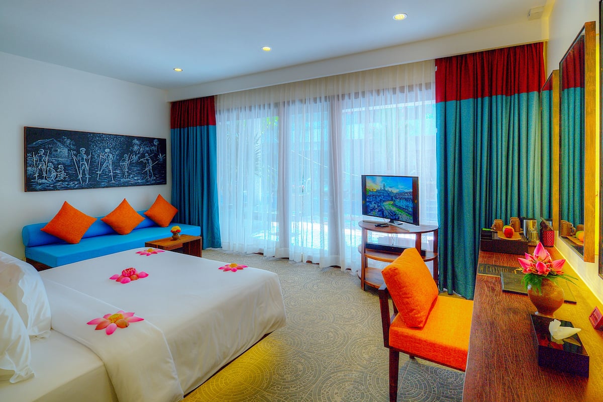 A hotel room with a bed, a blue sofa, a TV, and a desk.