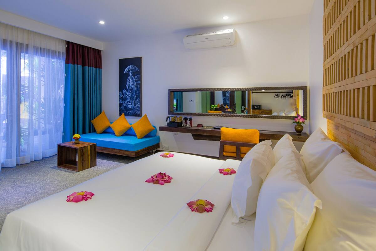 A hotel room with a large bed, a sofa with orange cushions, a desk, and a large mirror.