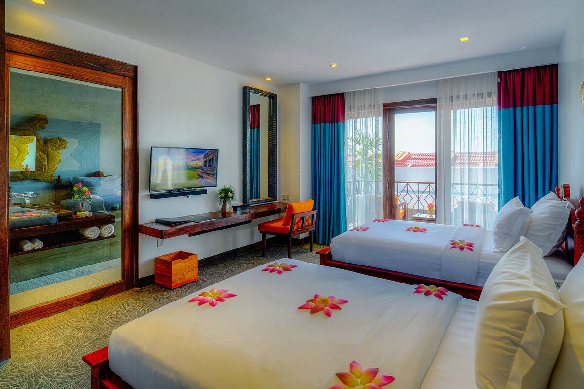 A hotel room with two beds, a TV, a desk, and a large mirror.