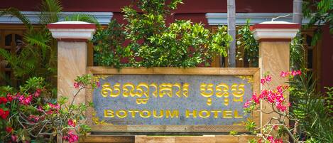 A sign for Botoum Hotel with a stone facade and potted plants.