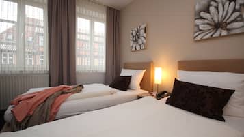 A hotel room with two beds, a window with curtains, and artwork on the wall.