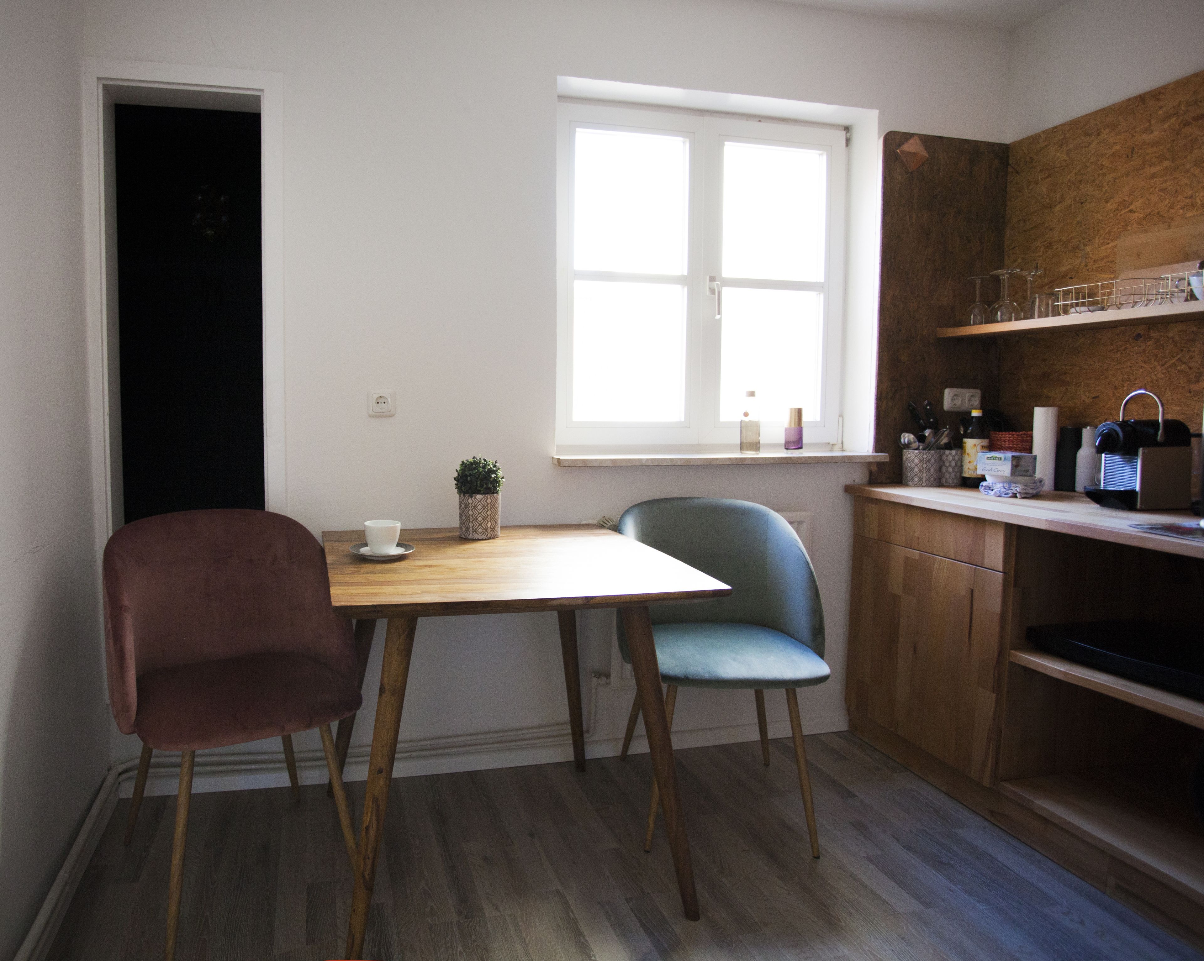 Una cocina pequeña con una mesa de madera, dos sillas, un ventanal y un armario de madera.