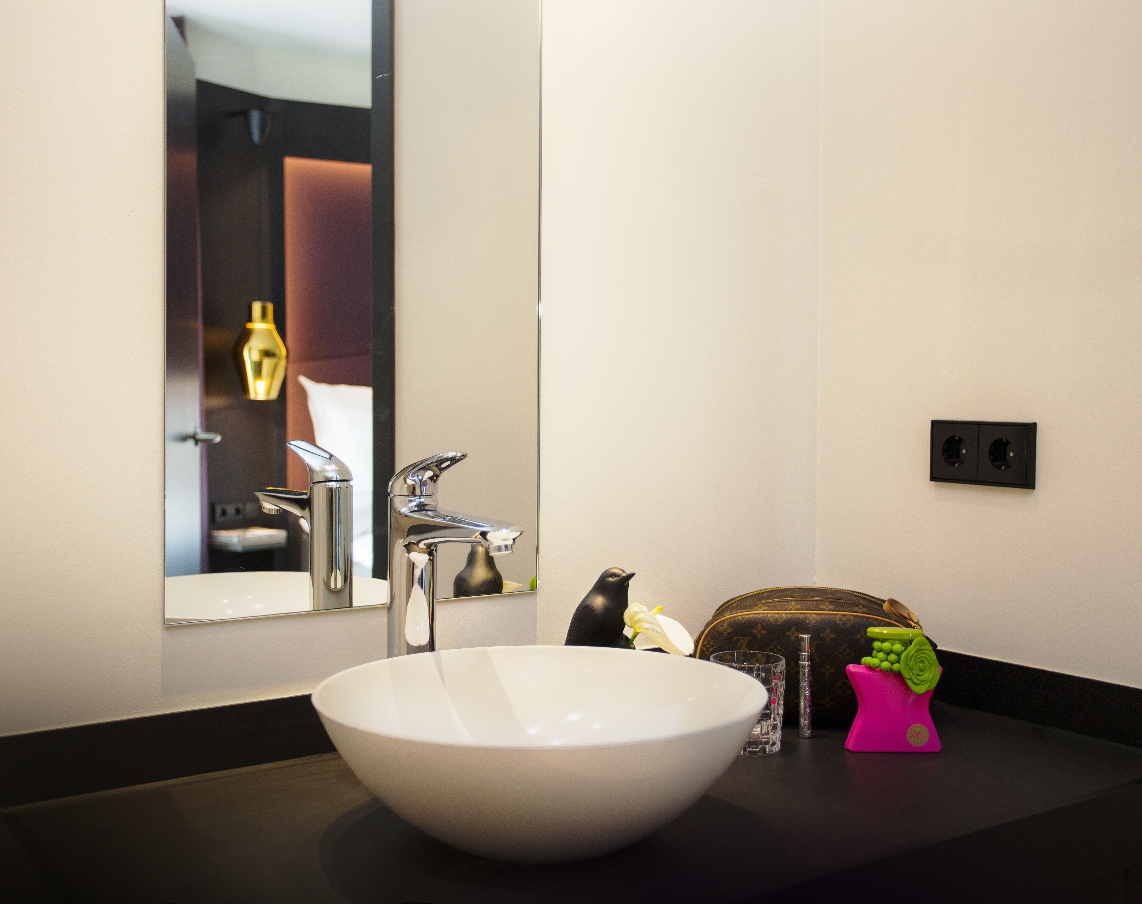 Un baño moderno con un lavamanos blanco, un espejo y una encimera negra.