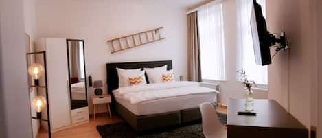 Un dormitorio moderno con una cama grande, mesitas de noche, un escritorio y un televisor montado en la pared.