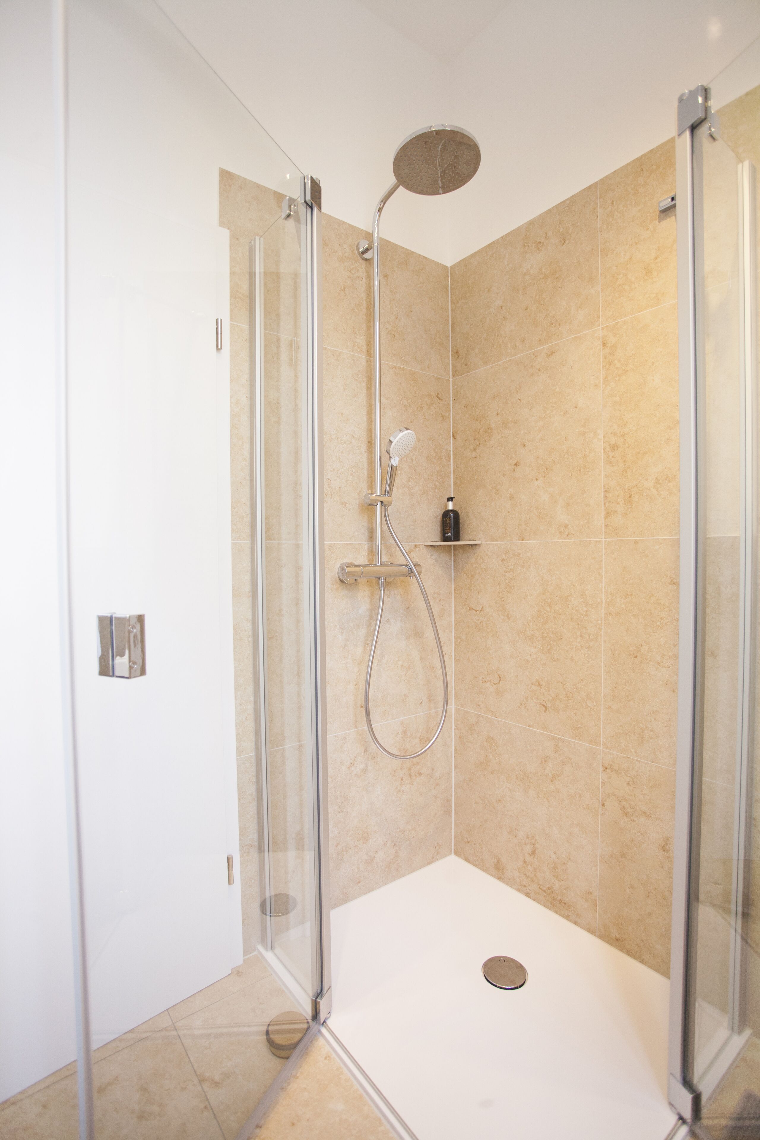 A modern shower with glass doors, a handheld showerhead, and a wall-mounted control panel.