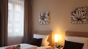 A hotel room with two beds, a nightstand with a lamp, and artwork on the walls.