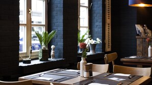 Interior de un restaurante con una mesa lista para comer, un jarrón con flores y una ventana con vistas a la calle.