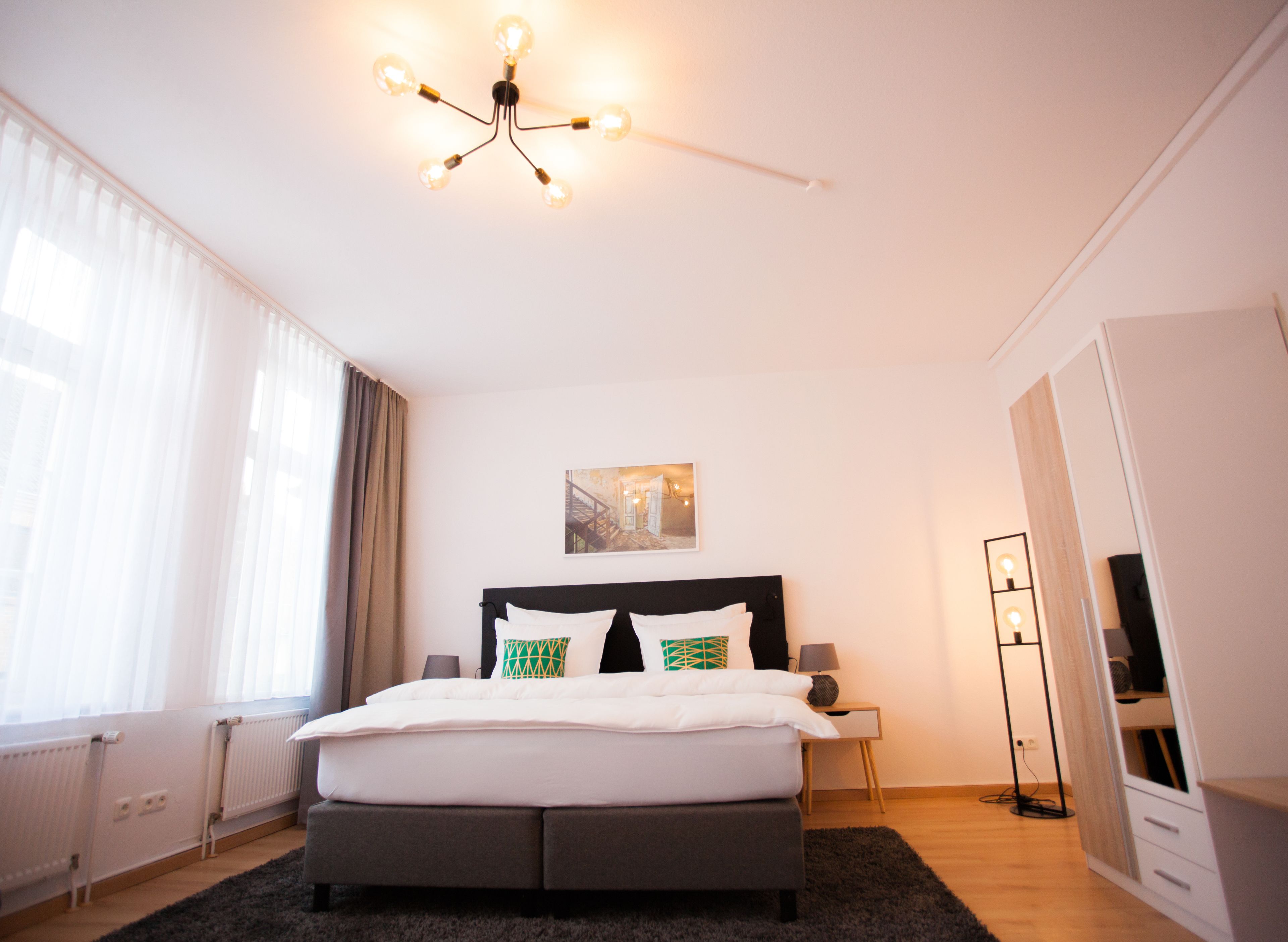 Un dormitorio moderno con una cama grande, un aplique de techo, una mesita de noche y una lámpara de pie.