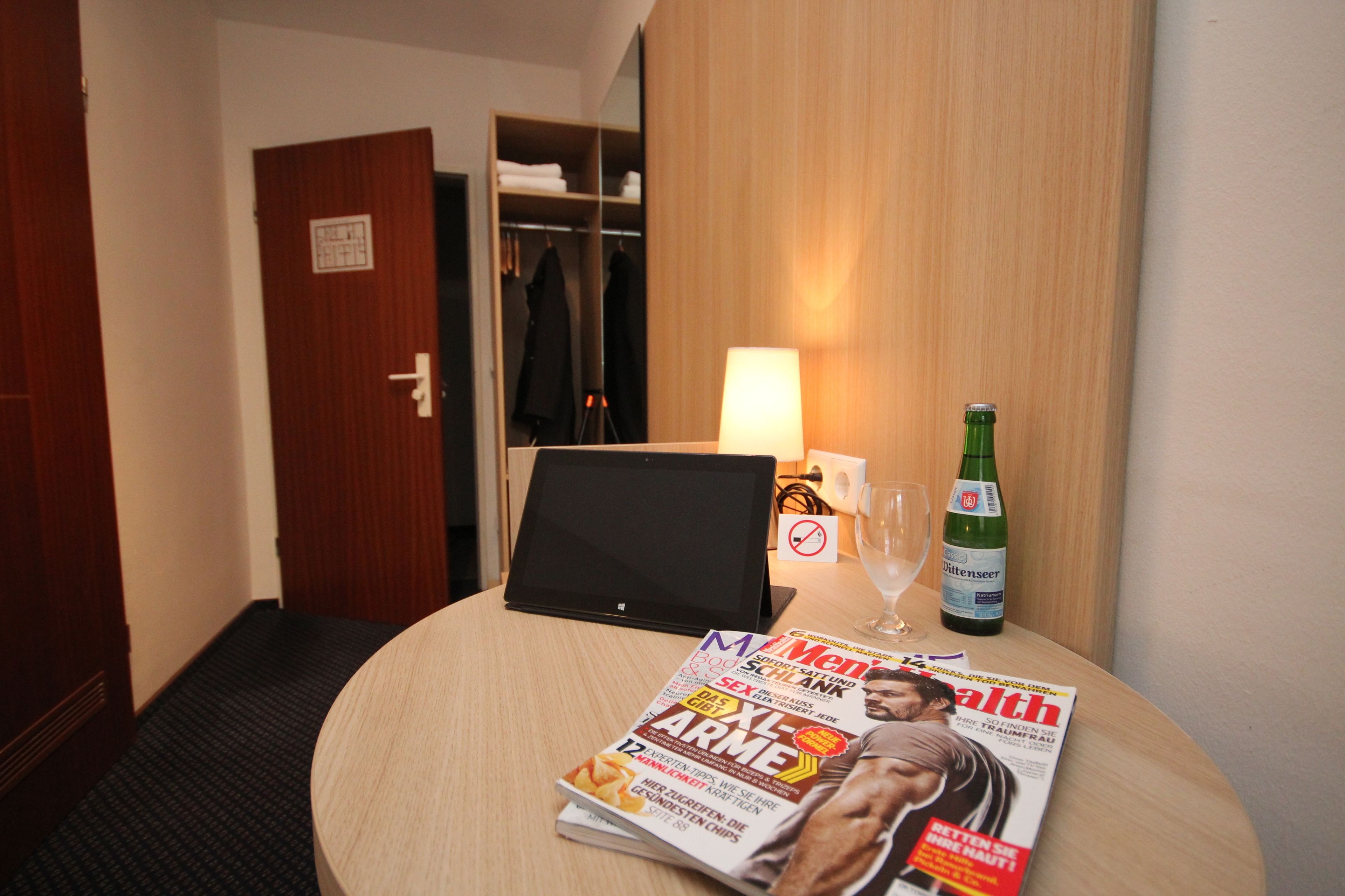 Une chambre d’hôtel avec une table ronde, un ordinateur portable, une bouteille de bière, un verre de vin et un magazine.