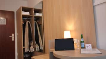 Una habitación de hotel con un armario de madera, una pequeña mesa de madera con una computadora portátil, una botella de agua y un vaso.