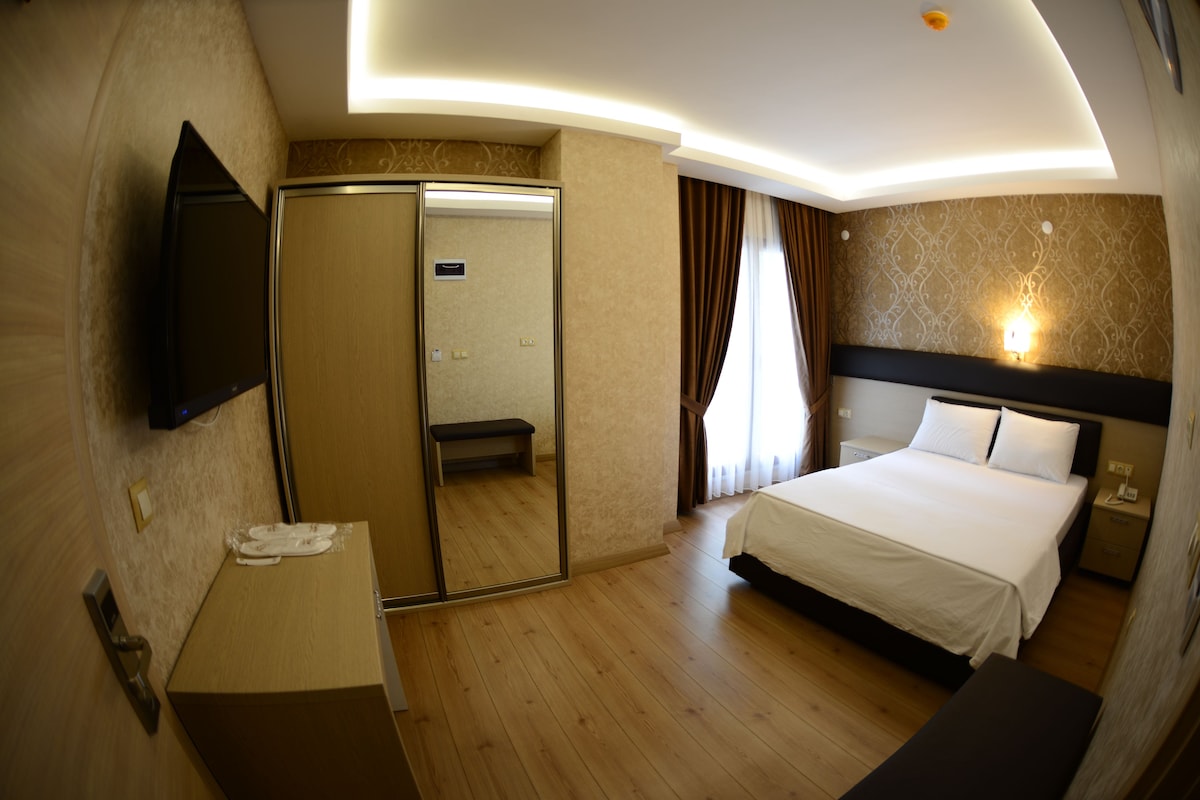 Una habitación de hotel con cama, mesita de noche, espejo y televisor montado en la pared.