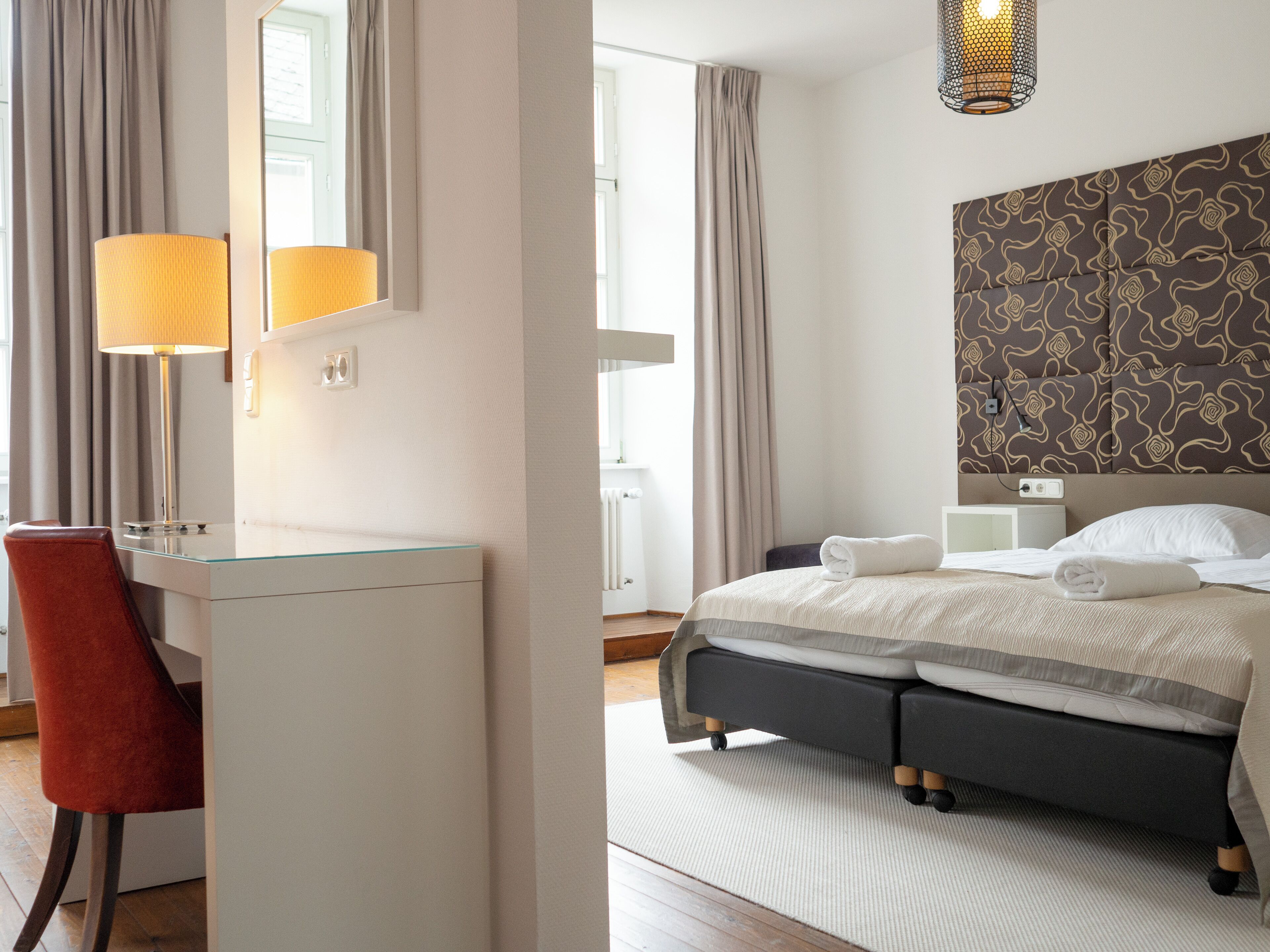 Et hotelværelse med skrivebord, stol, seng og sengegavl med mønster.