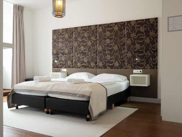 Une chambre d’hôtel moderne avec un grand lit, deux tables de chevet, un luminaire fixé au mur et une tête de lit à motifs.