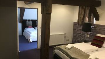 Et hotelværelse med træloft, en seng med hvide sengetøj og et sengebord med lampe, samt udsigt til et andet værelse.