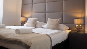 Habitación de hotel con un gran cabecero acolchado, dos mesitas de noche con lámparas, una cama bien tendida con una toalla enrollada y un aparador oscuro.