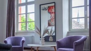 Una habitación con dos sillones morados, una mesa blanca con un florero y una obra de arte grande enmarcada.