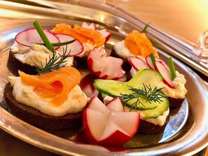 Un plato de aperitivos con salmón ahumado, aguacate, rábanos y queso crema sobre pan oscuro.
