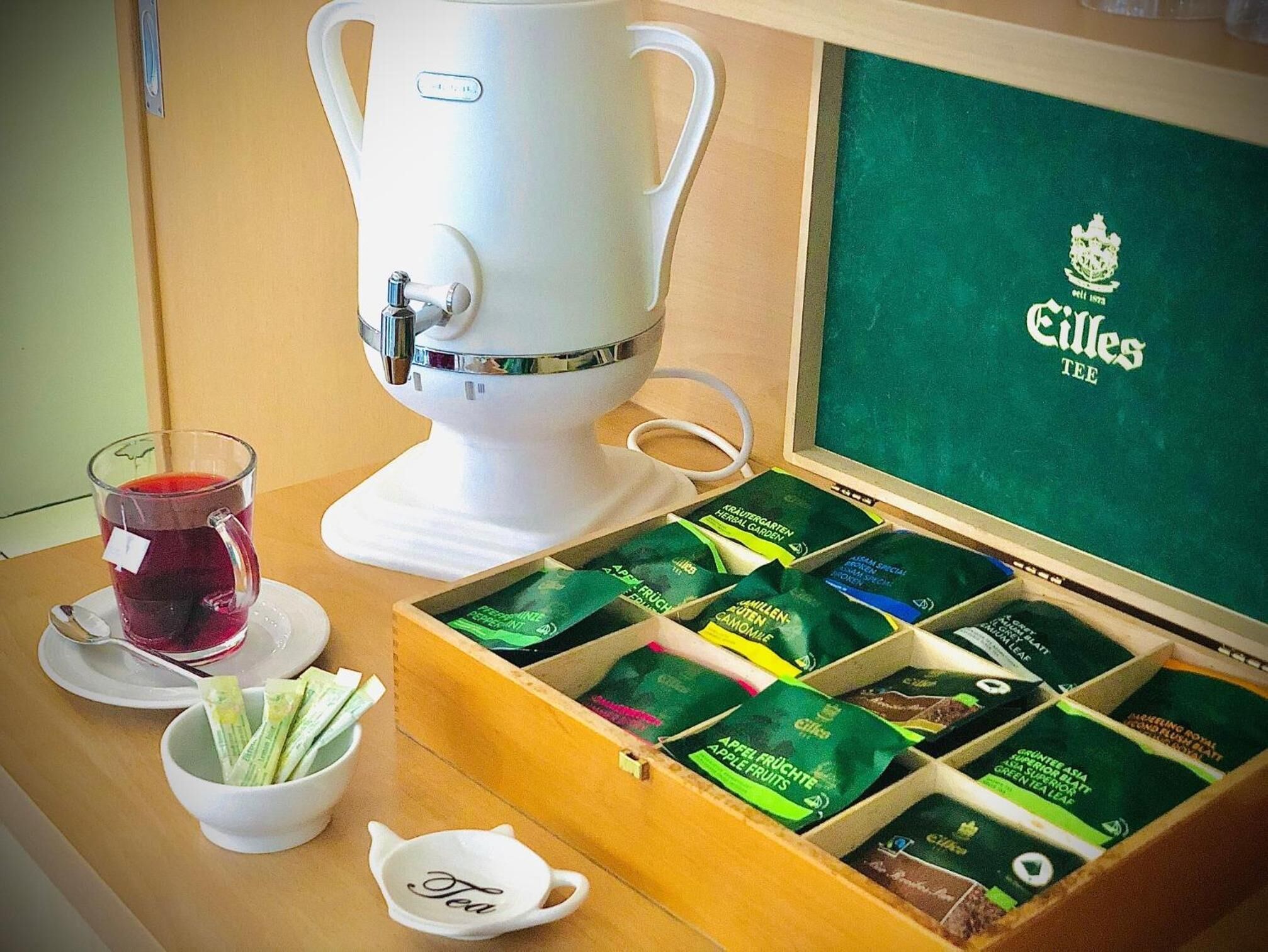 A coffee machine, a glass of tea, and a box of tea bags on a table.