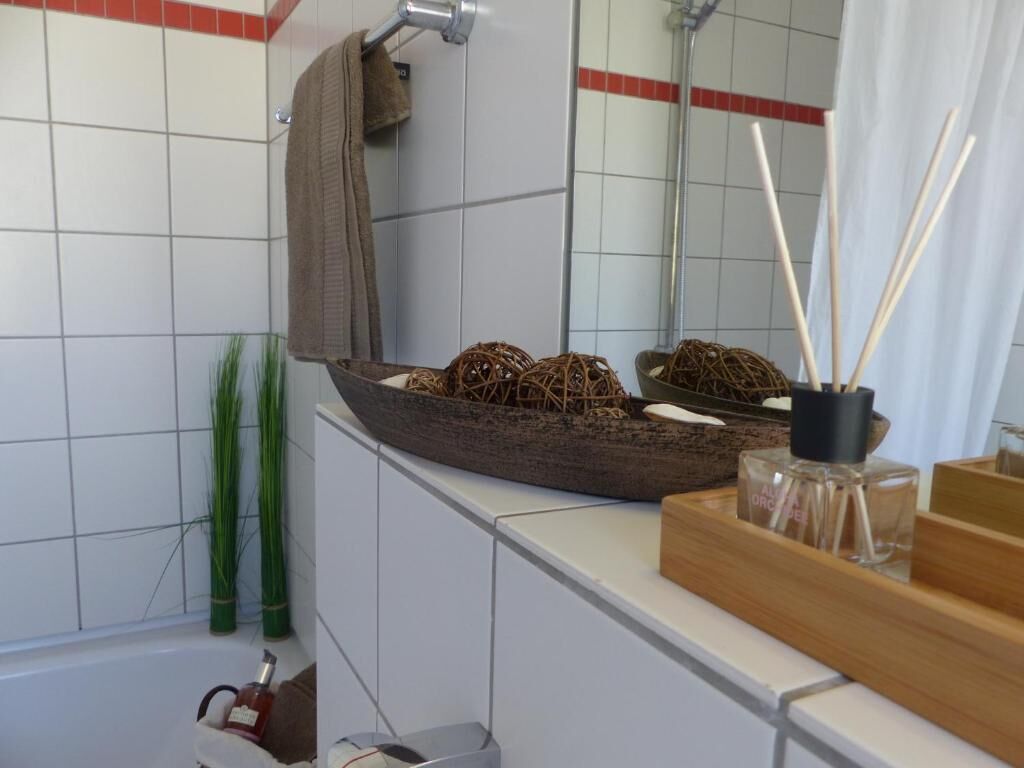 A bathroom with a large mirror, a wooden tray with decorative items, and a bottle of perfume on the counter.