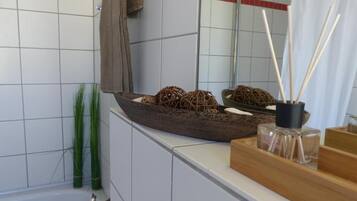 A bathroom with a large mirror, a wooden tray with decorative items, and a bottle of perfume on the counter.