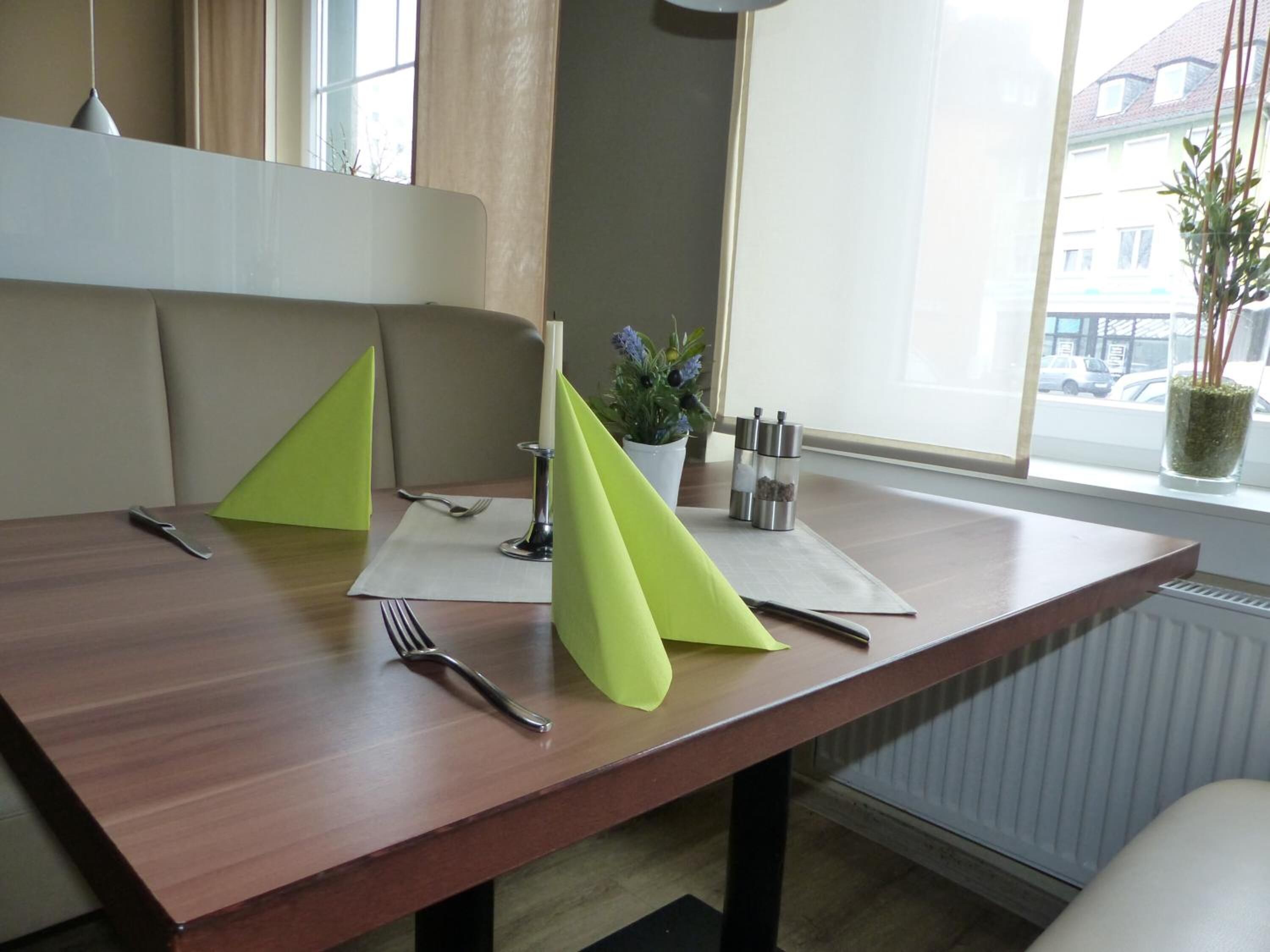 Una mesa de comedor con servilletas verdes, cubiertos y un candelabro.