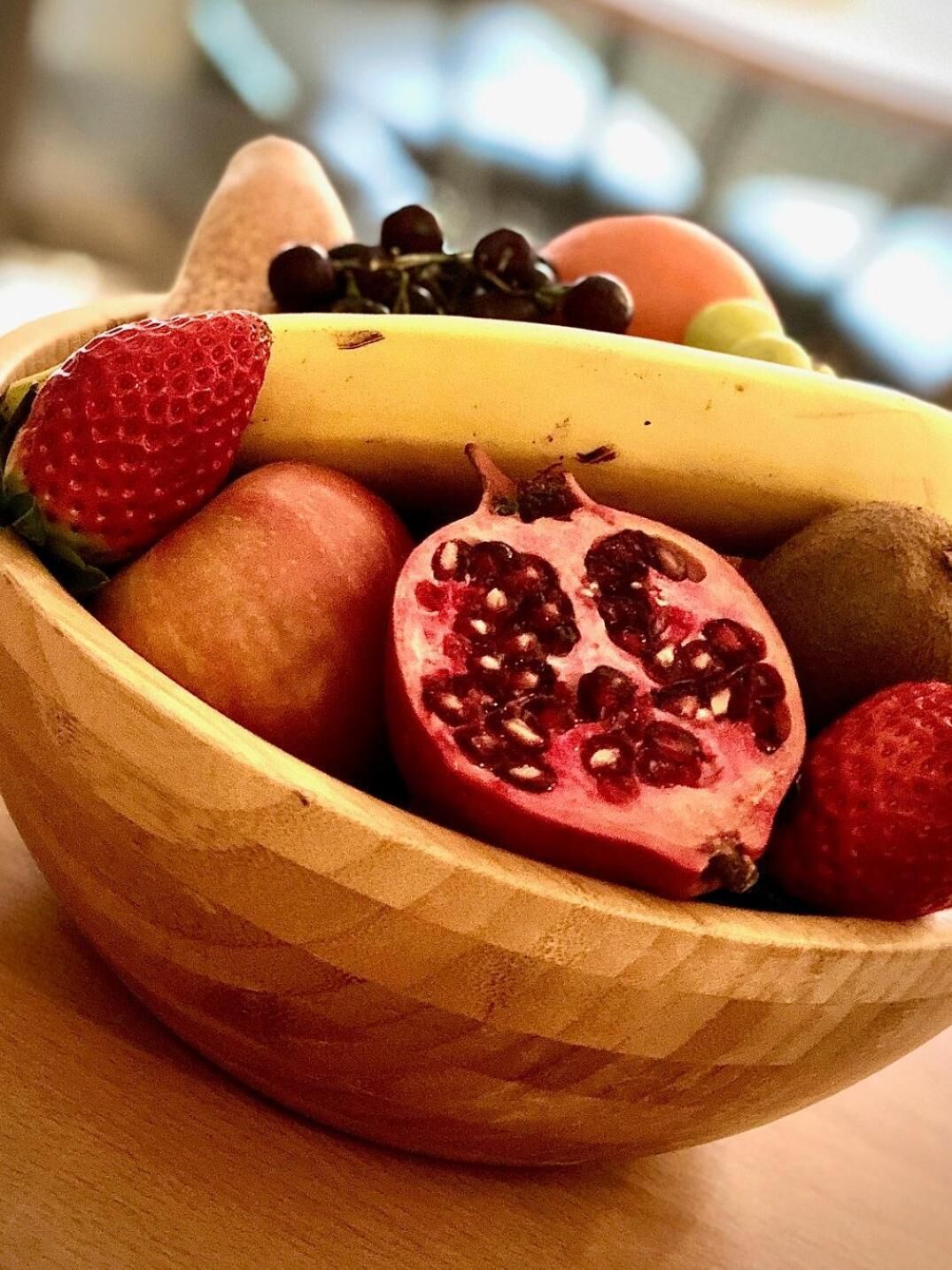 A wooden bowl containing a variety of fruits including strawberries, bananas, kiwis, and pomegranates.