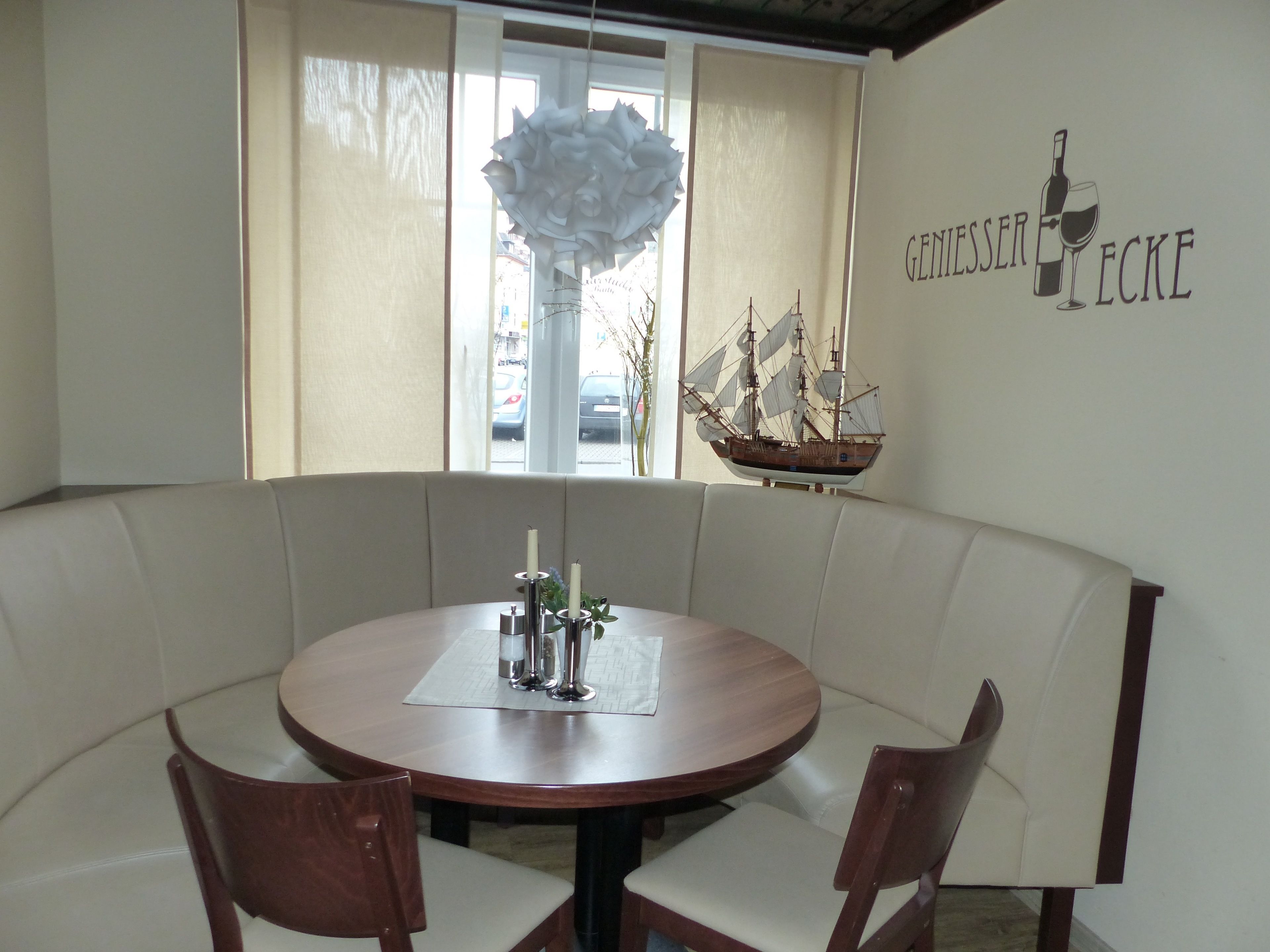 Un coin repas comprenant une table ronde, deux chaises, une maquette de bateau décorative et un panneau mural.