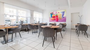 A modern cafe with round tables and grey chairs, large windows, and a colorful mural on the wall. - Hotel am Ludwigsplatz (Giessen)
