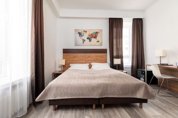 A modern hotel room with a large bed, a wooden headboard, a desk with a chair, a map artwork on the wall, and a view of the city through the window. - Hotel am Ludwigsplatz (Giessen)