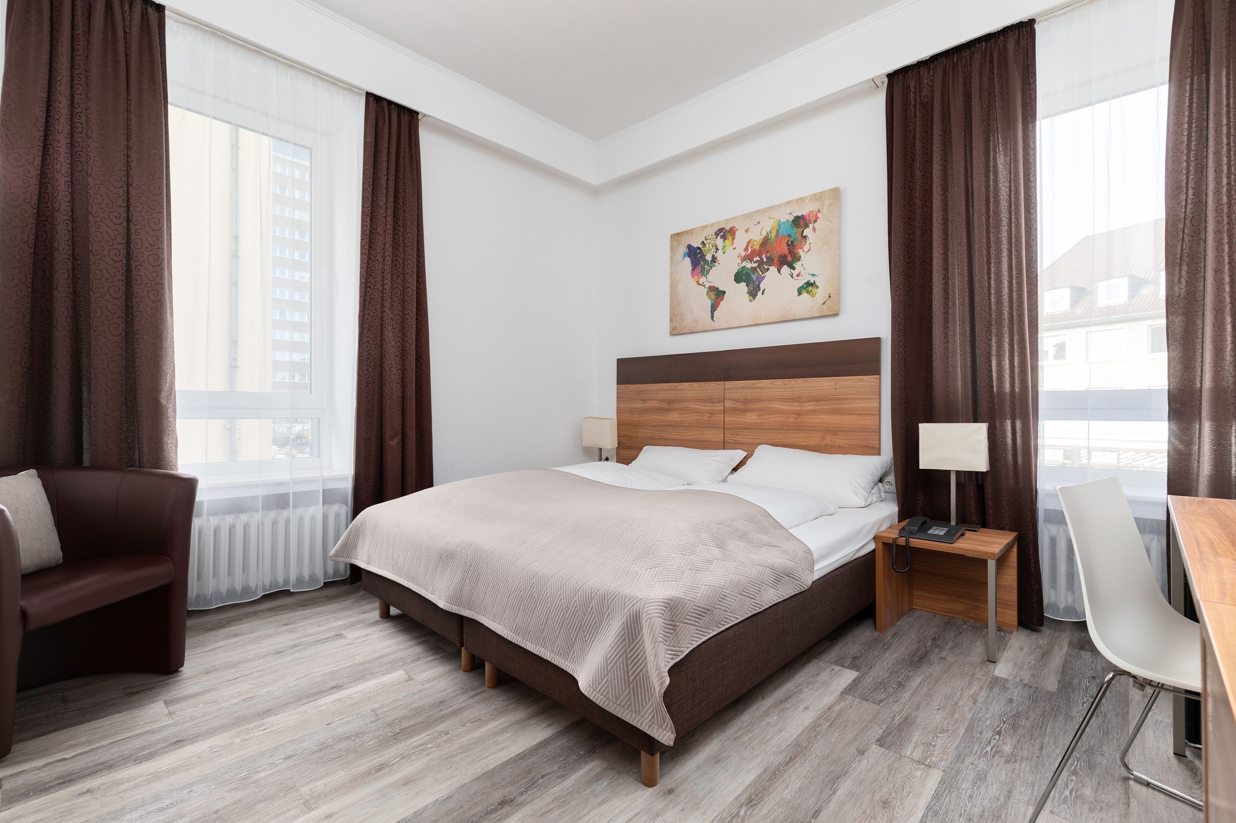 A hotel room with a large bed, a desk with a chair, a sofa, and a world map on the wall.