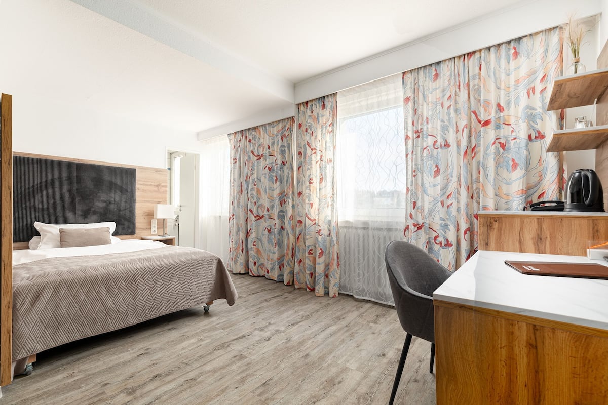 A hotel room with a bed, desk, chair, and curtains.
