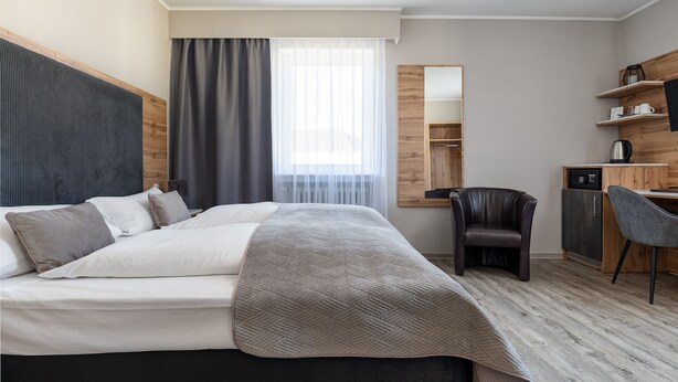 A modern hotel room with a large bed, a desk, a chair, and a wardrobe. - Hotel am Ludwigsplatz (Giessen)