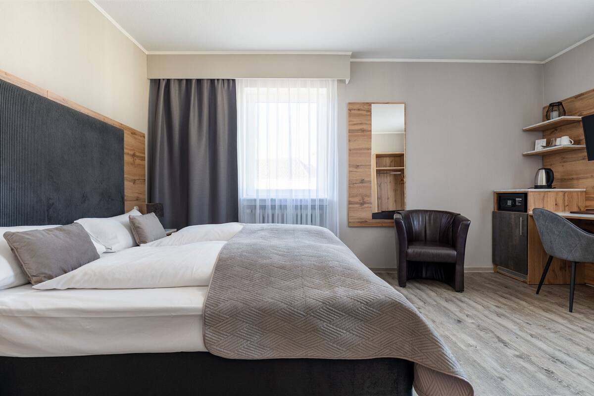 A modern hotel room with a large bed, a desk, a chair, and a wardrobe.