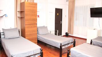A hotel room with three single beds, a wooden wardrobe, a television, and a desk.