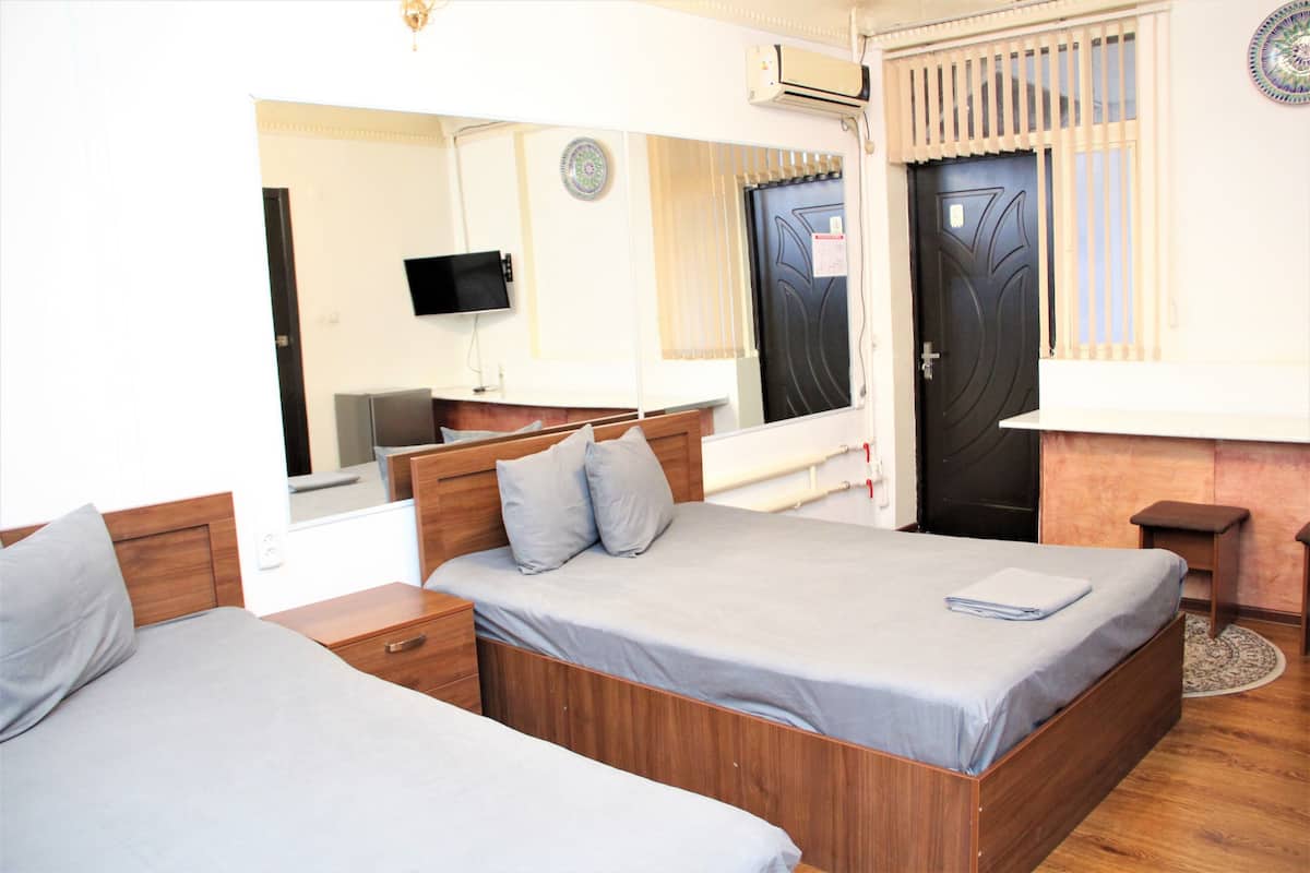 A hotel room with two beds, a TV, a mirror, and a door with a window.